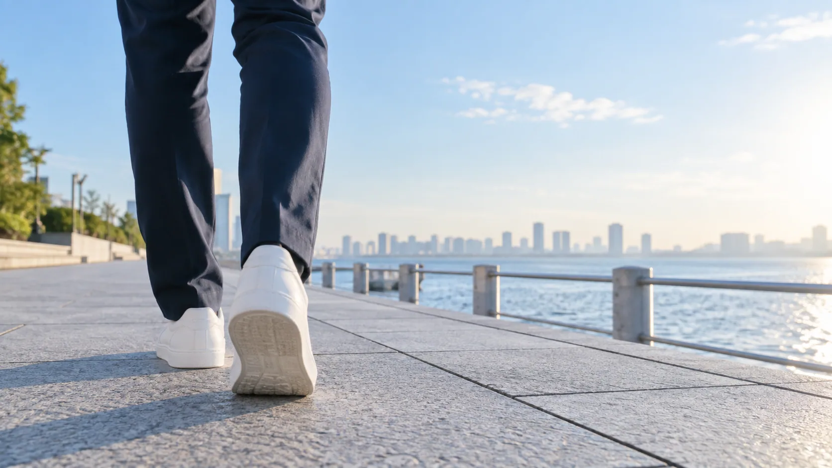 明るい海辺の道を白いスニーカーで歩く足元
